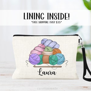 May include: A white canvas zippered pouch with a black zipper and a black strap. The pouch has a design of colorful yarn balls and a knitting needle with the name "Laura" printed below. The text "LINING INSIDE! *FREE SHIPPING OVER $35*" is printed at the top of the pouch.