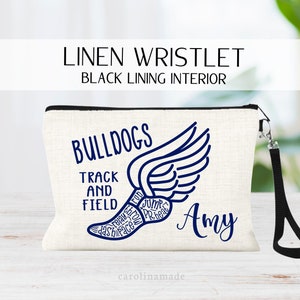 May include: A white linen wristlet with a black zipper and a black strap. The wristlet has a blue graphic of a running shoe with wings and the words "Bulldogs Track and Field" and "Amy".