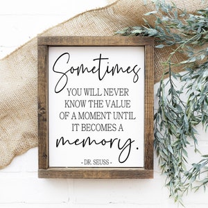 May include: A wooden sign with a white background and black text. The text reads "Sometimes you will never know the value of a moment until it becomes a memory. - DR. SEUSS -"