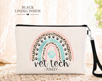 May include: A rectangular off-white canvas pouch with a black zipper and wrist strap. The front features a rainbow graphic with leopard print, teal, and pink stripes, small black paw prints, a teal paw print, and the text VET TECH - ASHLEY.