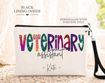 May include: A rectangular off-white canvas pouch with a black zipper and a black wrist strap. The front features the text VETERINARY assistant and the name Kate in black, with the word VETERINARY in a colorful leopard print pattern.