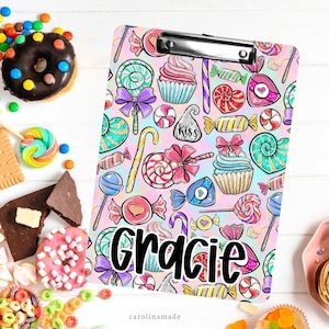 May include: A pink and blue clipboard with a candy and cupcake pattern. The name "Gracie" is written in black letters on the clipboard.