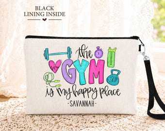 May include: A white rectangular zippered pouch with a black wrist strap. The front features colorful illustrations of gym equipment, a heart, and the text: the GYM is my happy place -SAVANNAH-. The text BLACK LINING INSIDE is printed above.