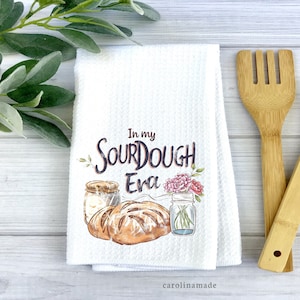 May include: White kitchen towel with the text "In my sourdough era" and a watercolor illustration of a loaf of sourdough bread, a jar of sourdough starter, and a mason jar with flowers.