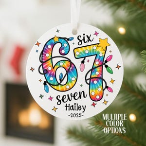 May include: A white, round Christmas ornament with the numbers "67" in a tie-dye pattern, surrounded by string lights. The ornament includes the words "six", "seven", "Hailey", and "-2025". The words "MULTIPLE COLOR OPTIONS" are also visible.
