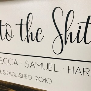 May include: White wooden sign with black calligraphy that reads "Welcome to the Shits - Rebecca - Samuel - Harpe Established 2010".