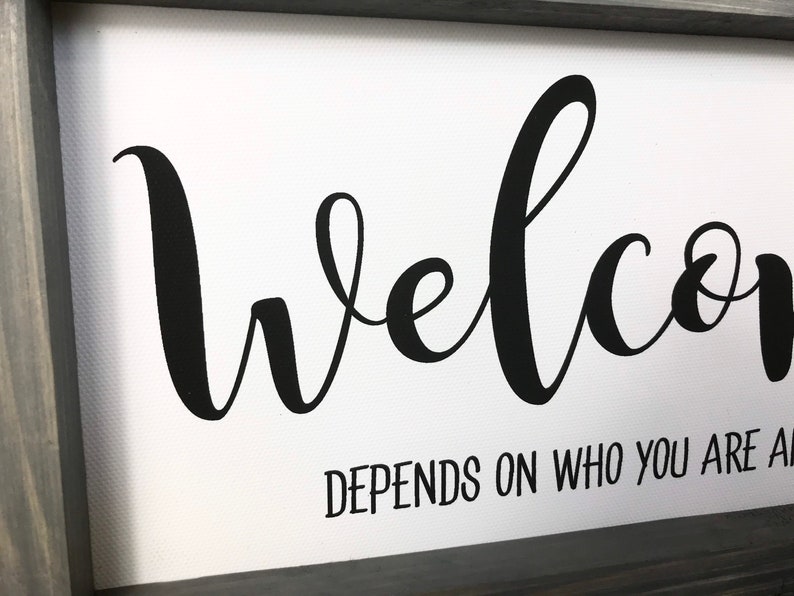 May include: A white canvas sign with a black cursive welcome sign and the text "depends on who you are asking" underneath.