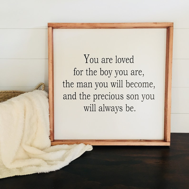 May include: A wooden sign with a white background and black text that reads "You are loved for the boy you are, the man you will become, and the precious son you will always be."