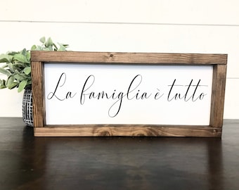 May include: A wooden sign with a white background and a brown frame. The sign says "La famiglia è tutto" in black cursive writing.