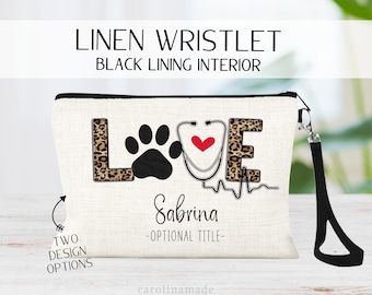 May include: Linen wristlet with black lining, featuring the word "LOVE" with a paw print, stethoscope, and heart design. The wristlet includes the name "Sabrina" and the text "Two Design Options". It has a black wrist strap.