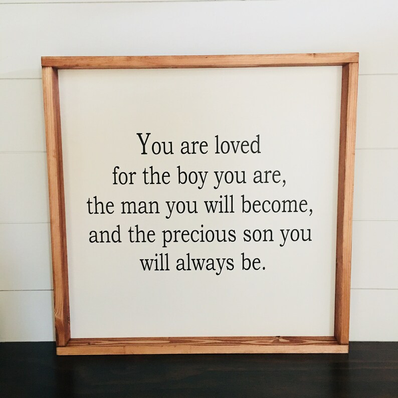 May include: A framed sign with a white background and a wooden frame. The sign reads "You are loved for the boy you are, the man you will become, and the precious son you will always be."