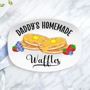 May include: White oval serving platter with the text "Daddy's Homemade Waffles" in black cursive font. The platter features a cartoon illustration of two stacks of waffles with butter and syrup.