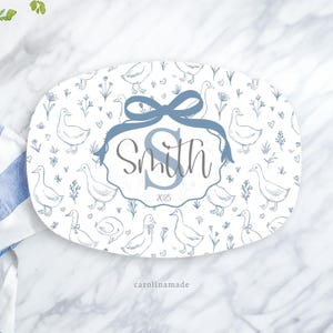 May include: An oval serving platter with a duck and floral pattern in blue and white. The platter features a blue ribbon and a personalized name and year. The text "Smith" and "2025" are displayed on the platter.