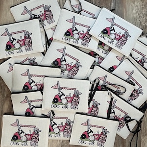May include: A collection of golf-themed cosmetic bags. Each bag features a pink golf cart with a golf ball, golf clubs, and the text "Chiks with Stiks" printed on a white background. The bags have black zippers and straps.