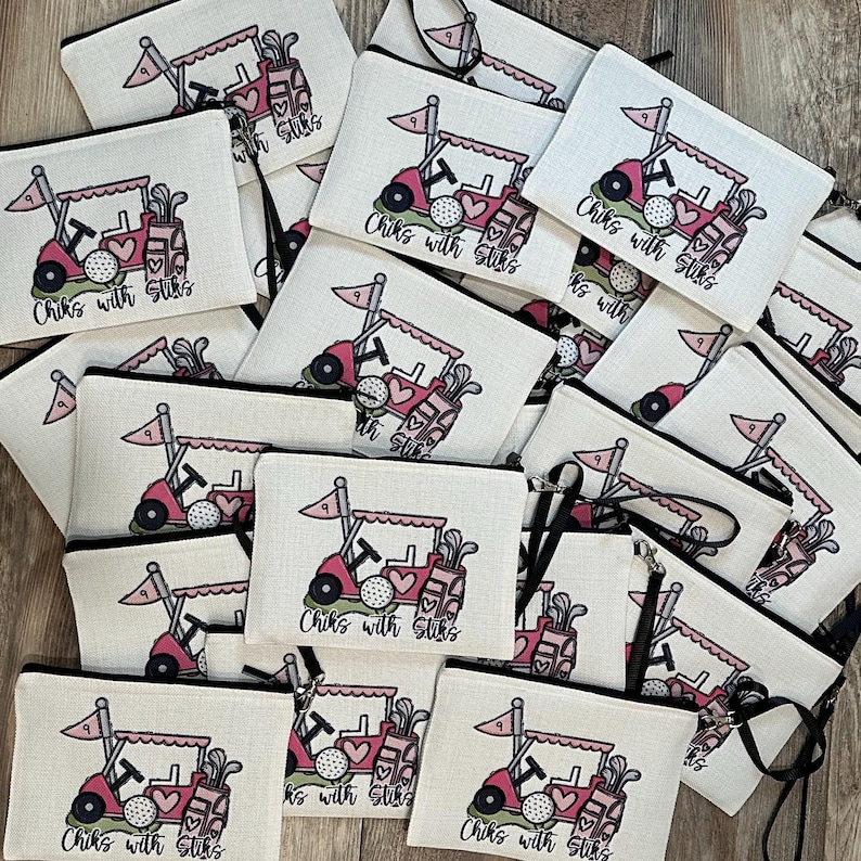 May include: A collection of golf-themed cosmetic bags. Each bag features a pink golf cart with a golf ball, golf clubs, and the text "Chiks with Stiks" printed on a white background. The bags have black zippers and straps.