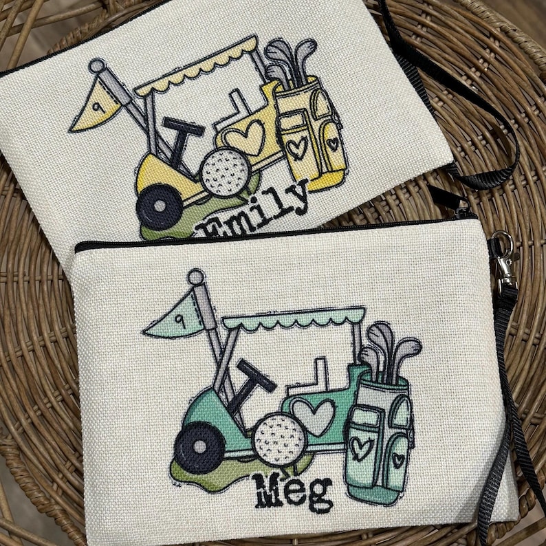 May include: Two canvas zipper pouches with golf-themed designs. One is yellow and the other is teal, both featuring golf carts, golf balls, and golf club bags. The yellow pouch has the word "family" and the teal pouch has the word "Meg".