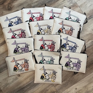 May include: A collection of golf-themed zippered pouches. Each pouch features a golf cart design with a golf ball, flag, and golf bag. The pouches are in various colors, including blue, red, green, and purple, with personalized names.