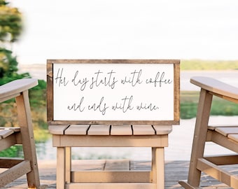 May include: A wooden sign with the text "Her day starts with coffee and ends with wine." The sign is sitting on a wooden table with two wooden chairs on either side.