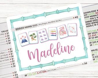 May include: A personalized Mahjong card featuring the name "Madeline" in pink script. The card has a light blue bamboo border and displays various Mahjong tiles with Japanese-inspired illustrations. The background is a light wood texture.