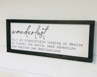 May include: A black framed sign with white background and the word "wanderlust" written in cursive. The definition of wanderlust is written below: "(n.) an irresistible longing or desire to travel the world, seek adventure and explore new destinations."
