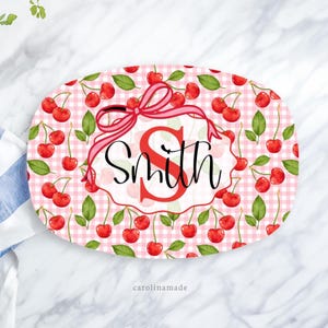 May include: Oval serving tray with a cherry pattern and the name "Smith" in a decorative font. The tray features a red gingham background, red cherries, green leaves, and a pink ribbon.