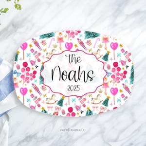 May include: Oval serving platter with a festive Christmas design. The white platter features a repeating pattern of pink and green Christmas elements, including nutcrackers, rocking horses, and Christmas trees. The center has the text "The Noahs 2025".