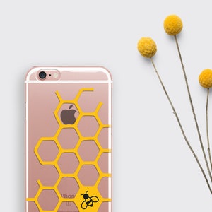 May include: A clear phone case with a honeycomb pattern and a small bee graphic. The case is pink and the honeycomb is yellow. The case is on a white background.