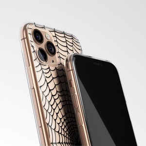 Peut inclure: Une coque de t&eacute;l&eacute;phone transparente avec un motif de toile d'araign&eacute;e noire. La coque est pr&eacute;sent&eacute;e sur un iPhone dor&eacute;.