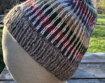 Könnte beinhalten: Eine gestrickte Mütze in Braun und Weiß mit einem bunten Muster. Die Mütze ist aus Wolle und hat eine dicke, warme Textur.