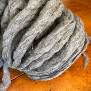 May include: A bundle of gray wool roving, tightly coiled and ready for crafting. The wool has a slightly textured appearance, with visible fibers and variations in color. The roving is a soft, muted gray, perfect for felting, spinning, or other fiber art projects.