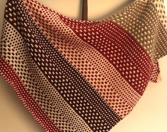 May include: A triangular knitted shawl with a striped pattern in shades of brown, red, and white. The shawl is made with a textured stitch that creates a dotted effect.