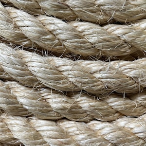 May include: Close-up of thick, beige rope with a textured surface. The rope is tightly wound, with visible strands and a natural, neutral color. The image highlights the rope's construction and texture.