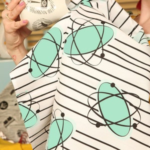 May include: A white tea towel with black stripes and a repeating pattern of turquoise atomic symbols. The text "Planet Sputnik Homestyle" is printed in the bottom left corner.