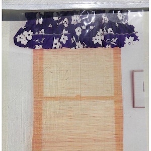 May include: A window valance featuring a dark purple fabric with a white floral pattern, attached to a light tan, woven, rectangular bamboo-style shade with a grid-like texture and a light orange border trim.