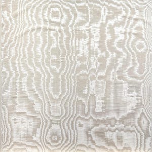 Op de afbeelding: Een close-up van een beige en wit patroonstof. Het ontwerp heeft een houtnerfpatroon met vloeiende, organische lijnen in tinten wit en beige. De stof heeft een zachte, getextureerde uitstraling.