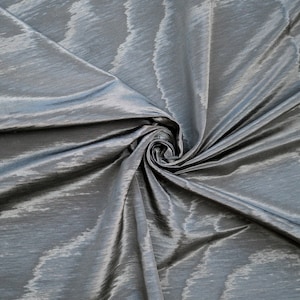 May include: Close-up of a silver fabric with a subtle shimmer and a textured pattern. The fabric is folded and draped, creating soft folds and curves.