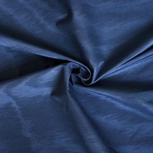 May include: Close-up of a navy blue fabric with a subtle sheen. The fabric is folded and draped, creating shadows and highlights that emphasize its texture. The material appears to be lightweight and flowing.