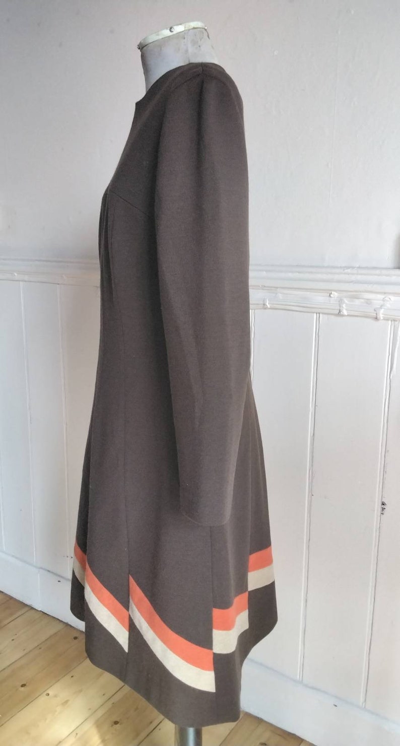 May include: A brown dress with a long sleeve and a white and orange stripe design at the hem.