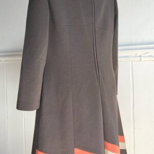 May include: A brown dress with a long sleeve and a back zip. The hem of the dress has a white and orange stripe design.