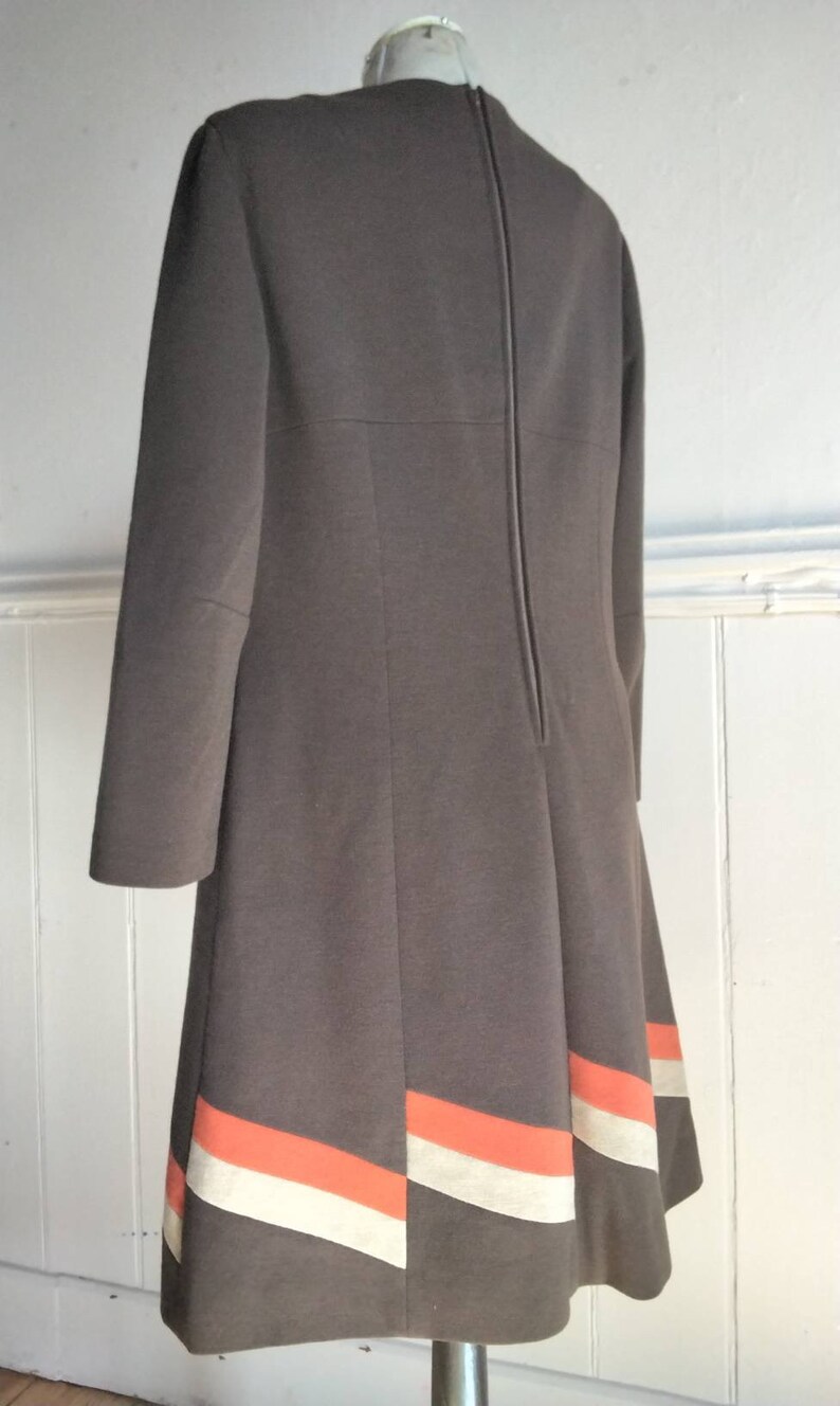 May include: A brown dress with a long sleeve and a back zip. The hem of the dress has a white and orange stripe design.