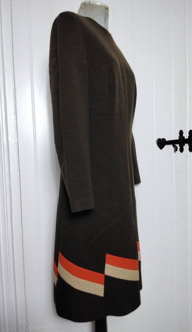 May include: A brown dress with a geometric pattern in orange and cream on the hem.