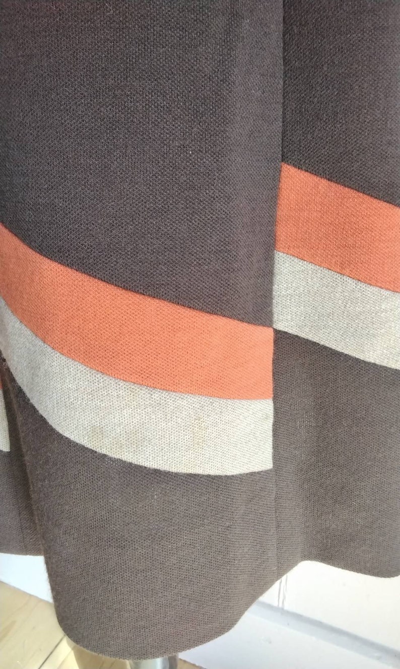 May include: A brown skirt with orange and beige stripes. The skirt is made of a woven fabric.