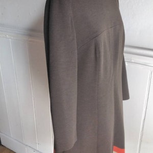 May include: A brown dress with a long sleeve and a white and orange stripe at the hem.