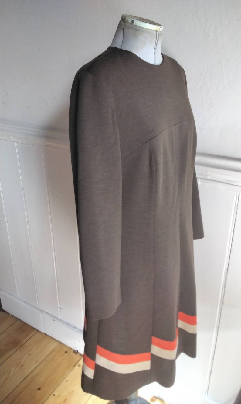 May include: A brown dress with a long sleeve and a white and orange stripe at the hem.