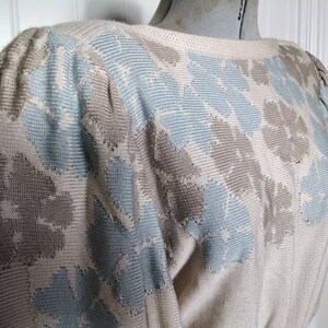May include: A cream-colored sweater with a blue and brown geometric pattern. The sweater has a round neckline and long sleeves.