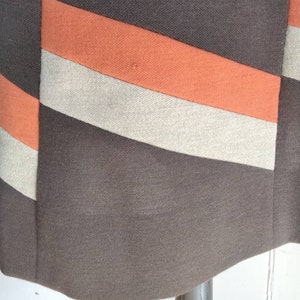 May include: A brown skirt with orange and beige stripes. The skirt is made of a textured fabric.