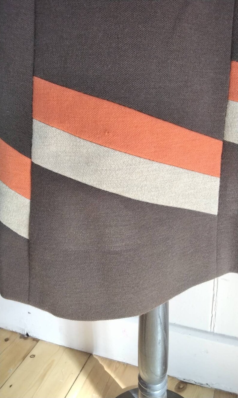 May include: A brown skirt with orange and beige stripes. The skirt is made of a textured fabric.