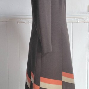 May include: A brown dress with a fitted bodice and a flared skirt. The skirt has a band of orange and beige trim at the hem.