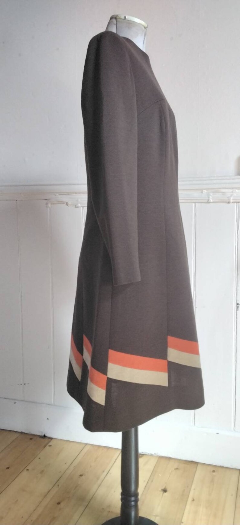 May include: A brown dress with a fitted bodice and a flared skirt. The skirt has a band of orange and beige trim at the hem.