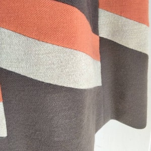 May include: Close-up of a brown, orange and beige striped fabric. The fabric has a woven texture.